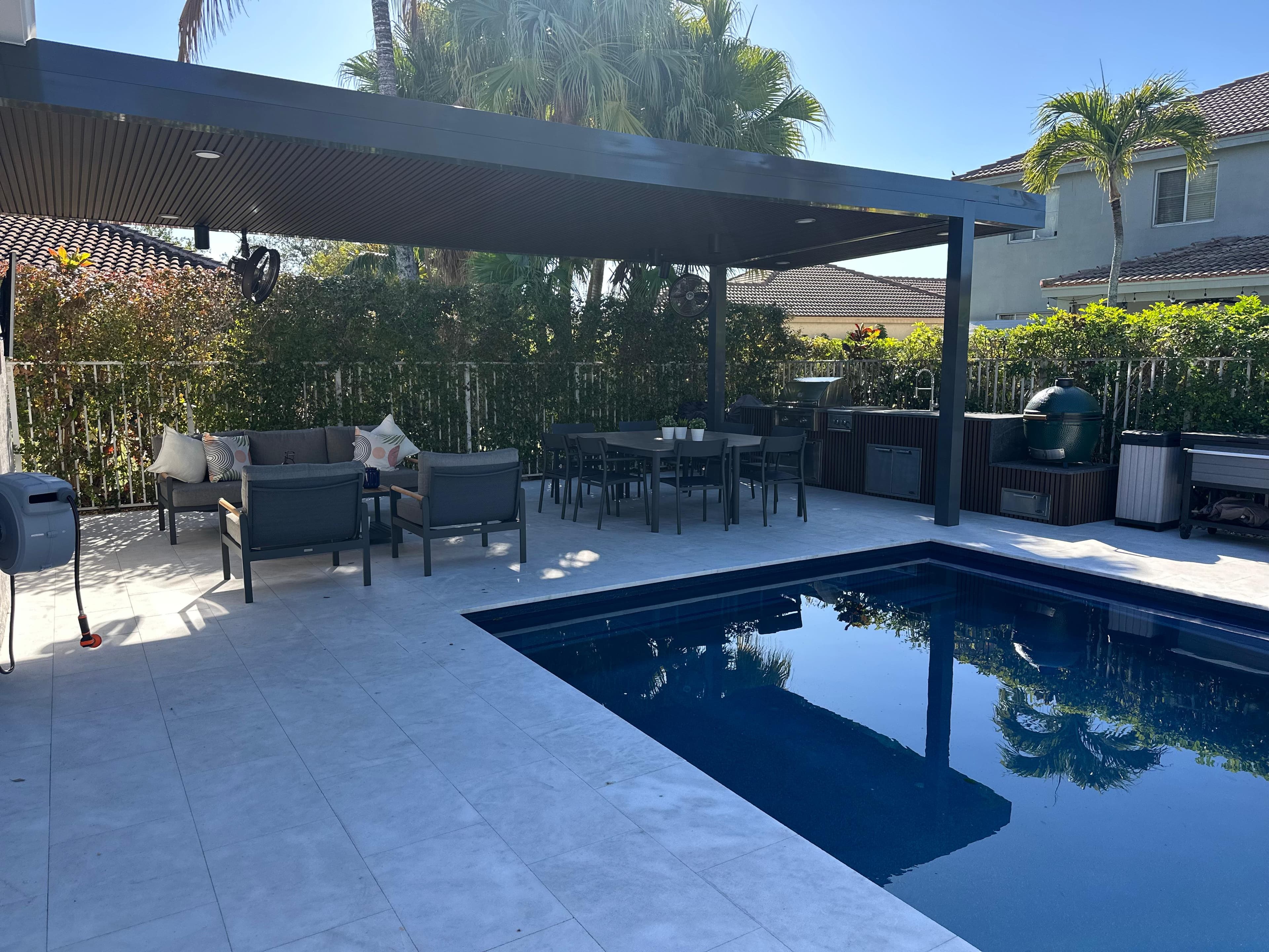 Covered patio with outdoor seating, dining area, and outdoor kitchen beside a modern pool in South Florida